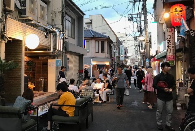 夕暮れ時の福山駅前の一角。雑居ビルをリノベーションした飲食店の店先にソファを出して食事を楽しむ人々の写真(外部ページへリンク。別ウィンドウで開きます）(別ウィンドウで開きます)