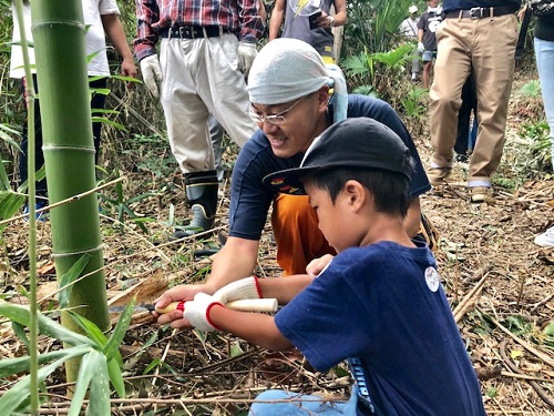 大人と子どもが一緒にノコギリで竹を切っている写真