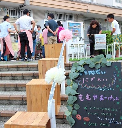 ももやまーけっとの看板の前で、団地にお住まいの方が交流をしている写真