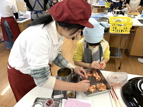 参加者の子供と一緒に調理体験でエビの皮をむいている大学生の写真
