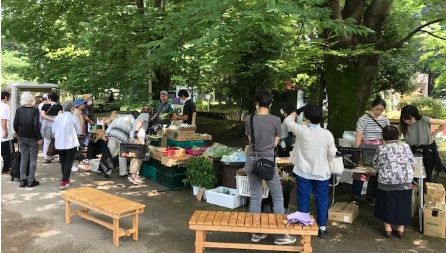 木陰にたくさんの野菜などの商品が並べられている写真