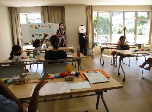 教室で先生の話を聞いて、手を挙げている子供たちの写真