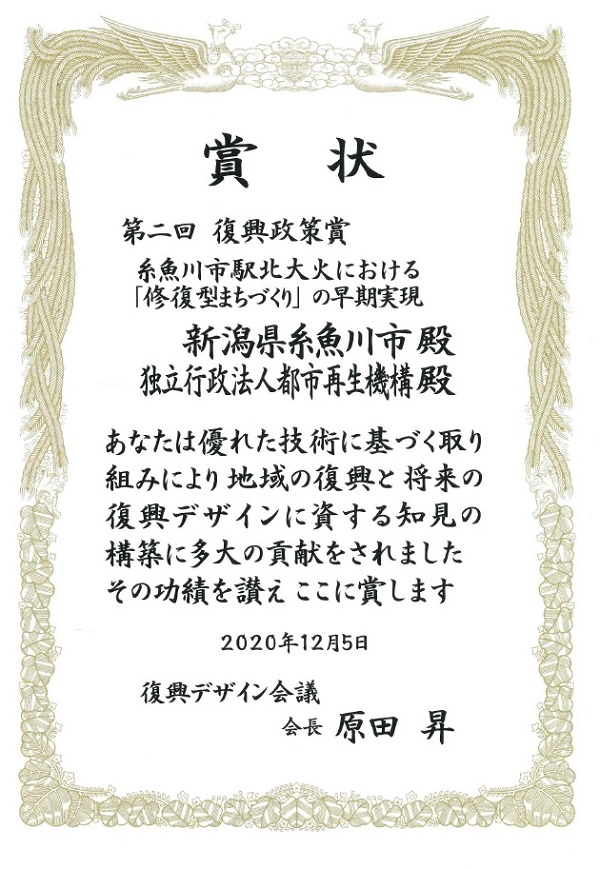 賞状　第二回復興政策賞　糸魚川市駅北大火における「修復型まちづくり」の早期実現　新潟県糸魚川市殿　独立行政法人都市再生機構殿　あなたは優れた技術に基づく取り組みにより地域の復興と将来の復興デザインに資する知見の構築に多大の貢献をされました　その功績を讃えここに賞します　2020年12月5日　復興デザイン会議　会長　原田昇