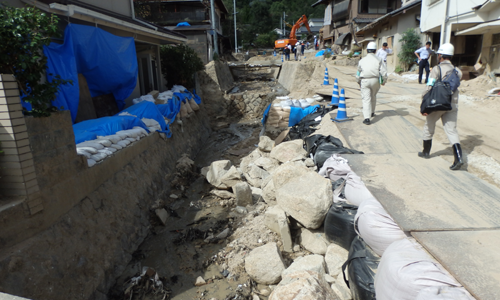 土砂や石が流れ込んだ家の前で被害状況を確認するUR職員の写真