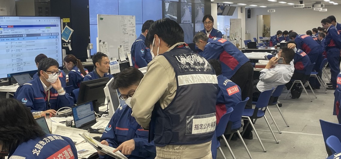 災害対応のための指令室で、UR都市機構を含む関係者が情報共有・調整を行っている写真