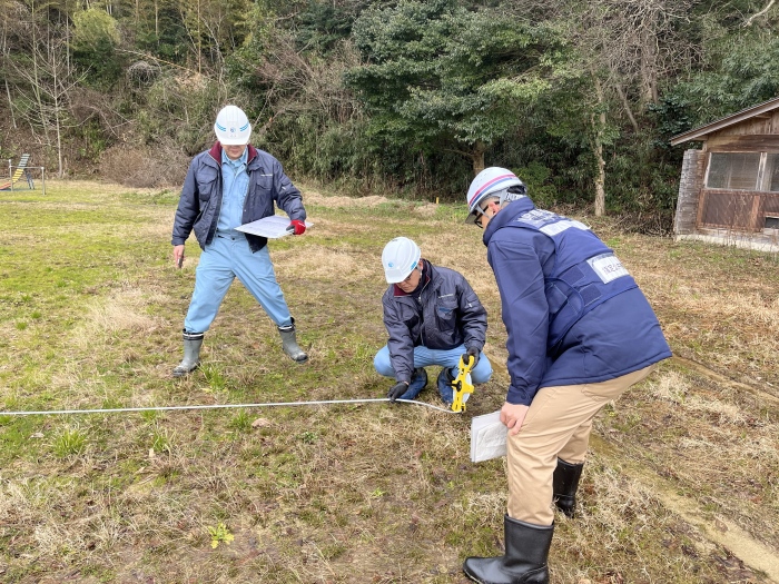 調査員が屋外でロープと測定器を使い、敷地の寸法を測量している場面。