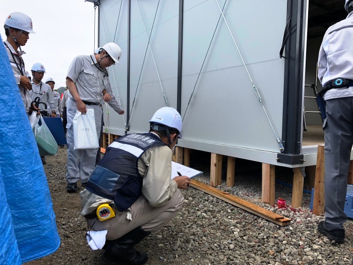 UR都市機構と書かれた服を着た調査員が仮設建物の基礎部分を点検し、記録している様子。