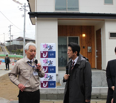 写真：安倍首相へ住宅の前で説明するＵＲ小山震災復興推進役（左）