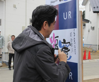 写真：写真：看板にサインをされる安倍首相