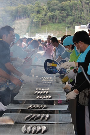 写真:次々と焼かれる秋刀魚。香ばしい香りが会場に広がります <次々と焼かれる秋刀魚。香ばしい香りが会場に広がります>