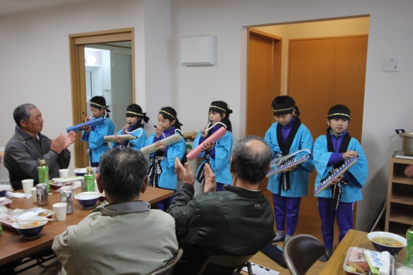 写真：浦戸第二小学校の児童による歌、演奏の披露。大人も笑顔で手拍子