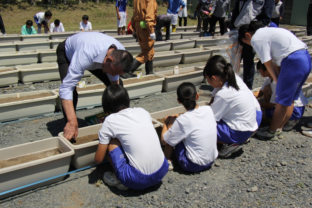 写真：山田中学校の生徒らと種まきをするグレート小鹿さん（左）