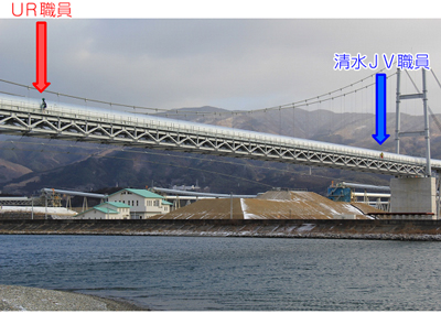 写真:トレッカーを背負って気仙川にかかる「希望のかけ橋」を渡るUR職員と先導する清水JV職員