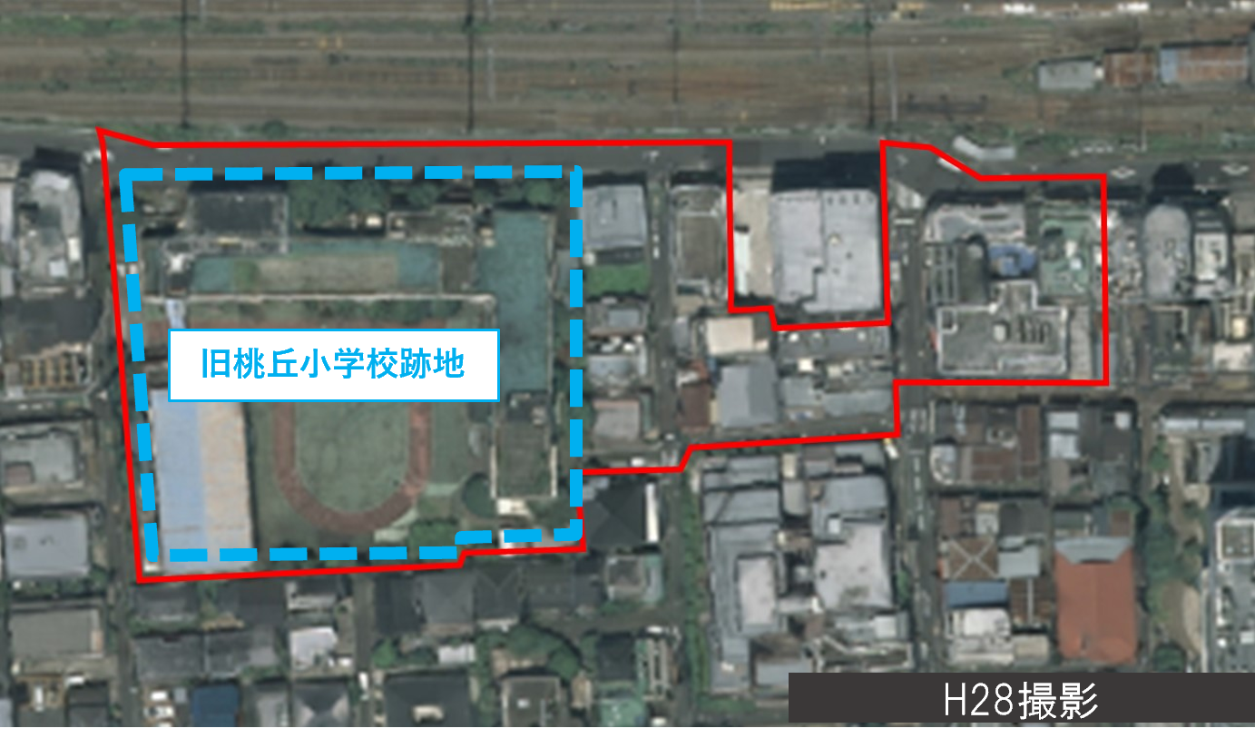H28年度撮影　旧桃丘小学校跡地を含む再開発エリアの航空写真。赤枠で事業区域、青破線で旧桃丘小学校跡地を示す。